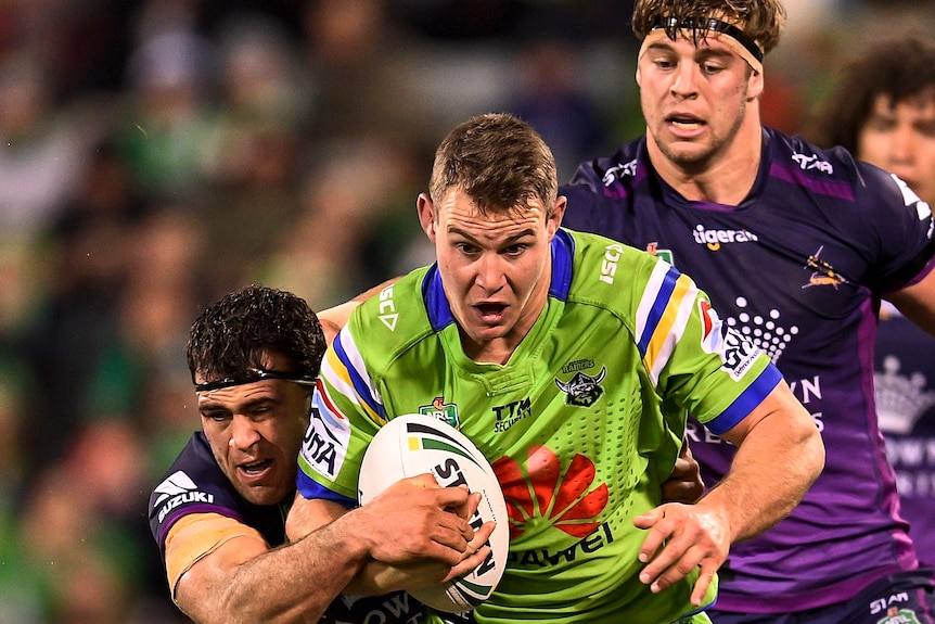 NRL player Luke Bateman, wearing green, is tackled by two Melbourne Storm players.