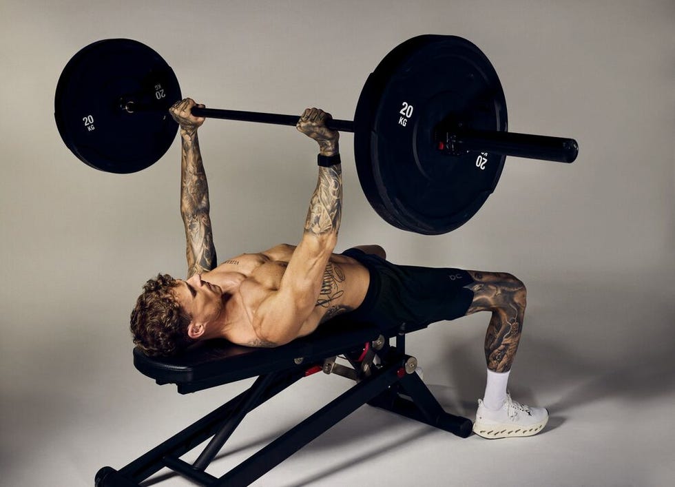 person performing a bench press with tattoos visible on arms and legs.