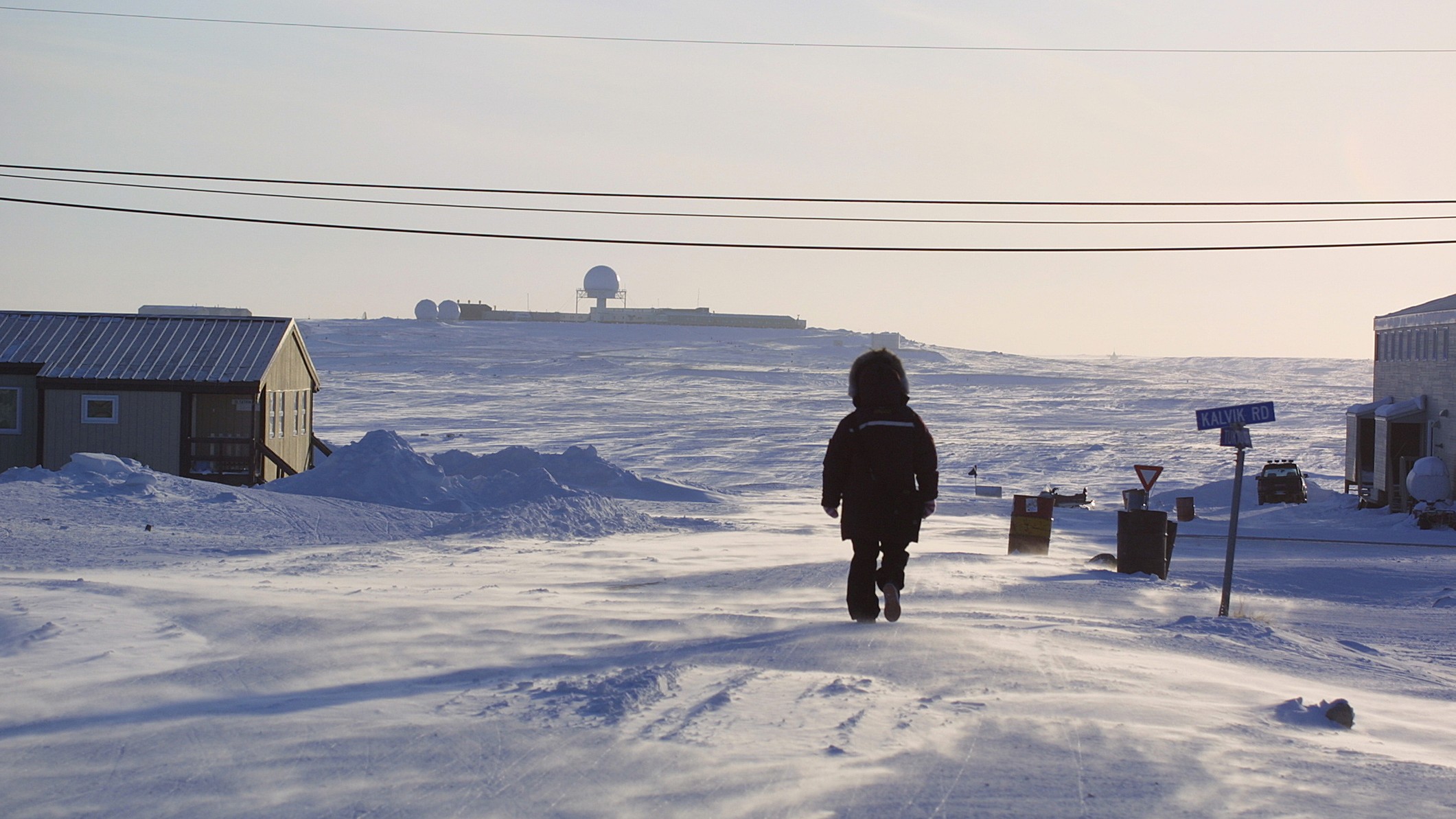 A person walking through snow toward an air defence radar station in Cambridge Bay, Nunavut.