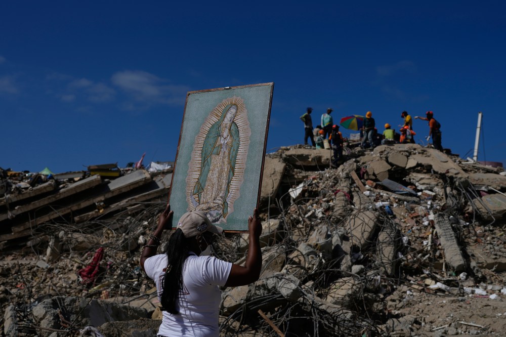 A woman holds a painting of the Virgin Mary as she accompanies a Catholic priest supporting people searching for the remains of relatives in the rubble of residential buildings that collapsed during the earthquakes that struck La Guaira, Venezuela, Friday, July 17, 2026. (AP Photo/Ariana Cubillos)