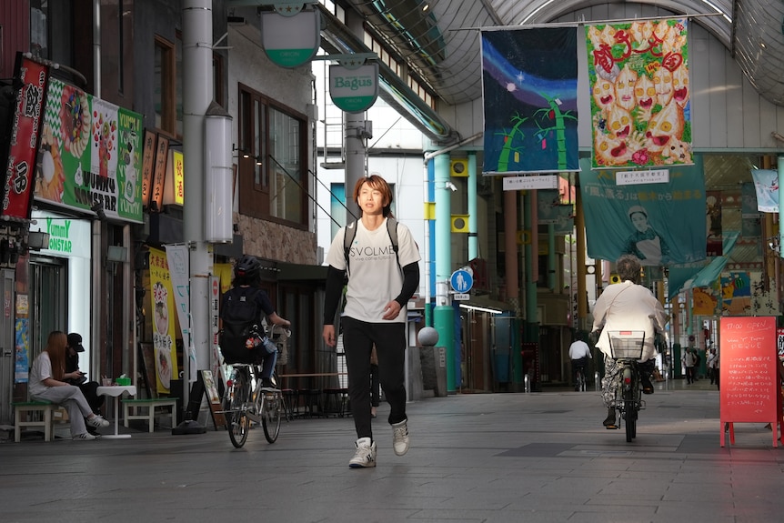 A man in a white t-shirt walks through a shopping arcade