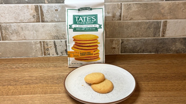 Two Tate's Lemon Cookies on a white plate with the box in the back leaning on the counter