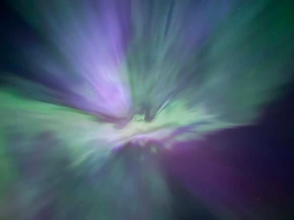 Vibrant streaks of green and purple aurora light converge overhead, creating a spectacular celestial display across the night sky. Photo Amanda Esligar Keating