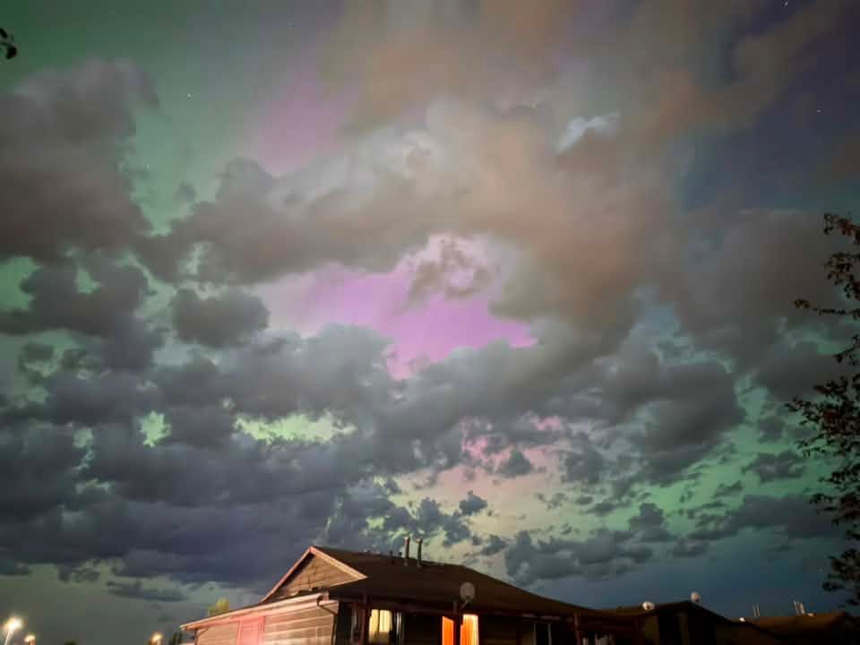 Purple and green hues of the aurora borealis glow through a break in the clouds above a neighbourhood skyline during a dramatic late-night light show. Photo Bryson Wereschuk