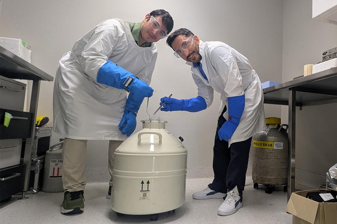 Two scientists posing with a liquid nitrogen storage cannister in a laboratory.