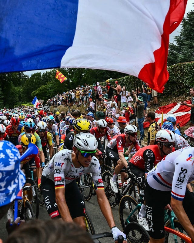 Professional cyclists racing with spectators cheering and waving flags along a scenic course. Professional cyclists racing with spectators cheering and waving flags along a scenic course.