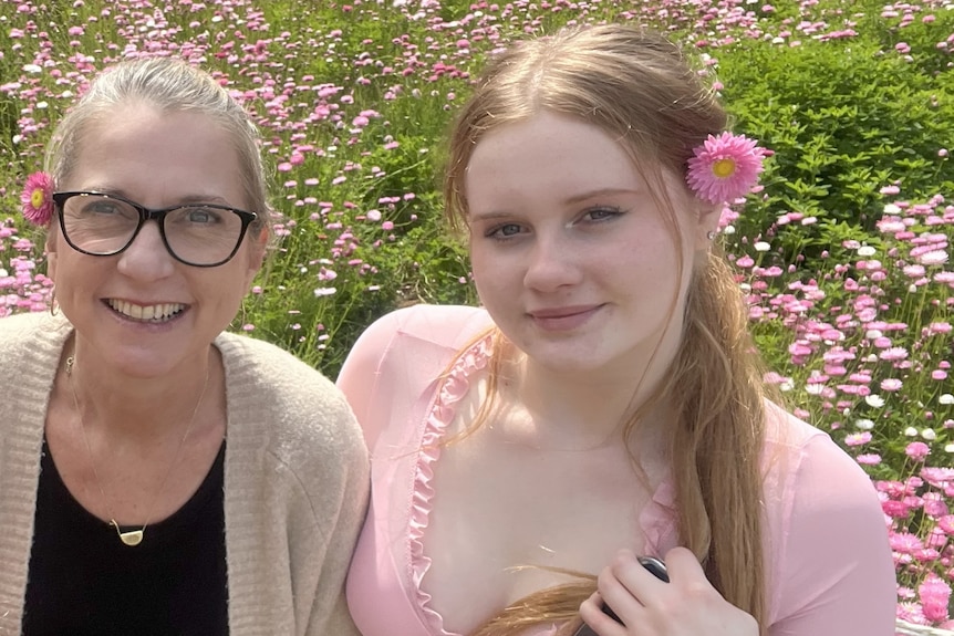 Two women pose for a photo in an orchid of pink flowers