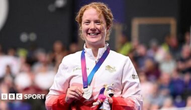 Morgan Newberry stands on the podium with her silver medal in her hand and holding a small mascot toy.