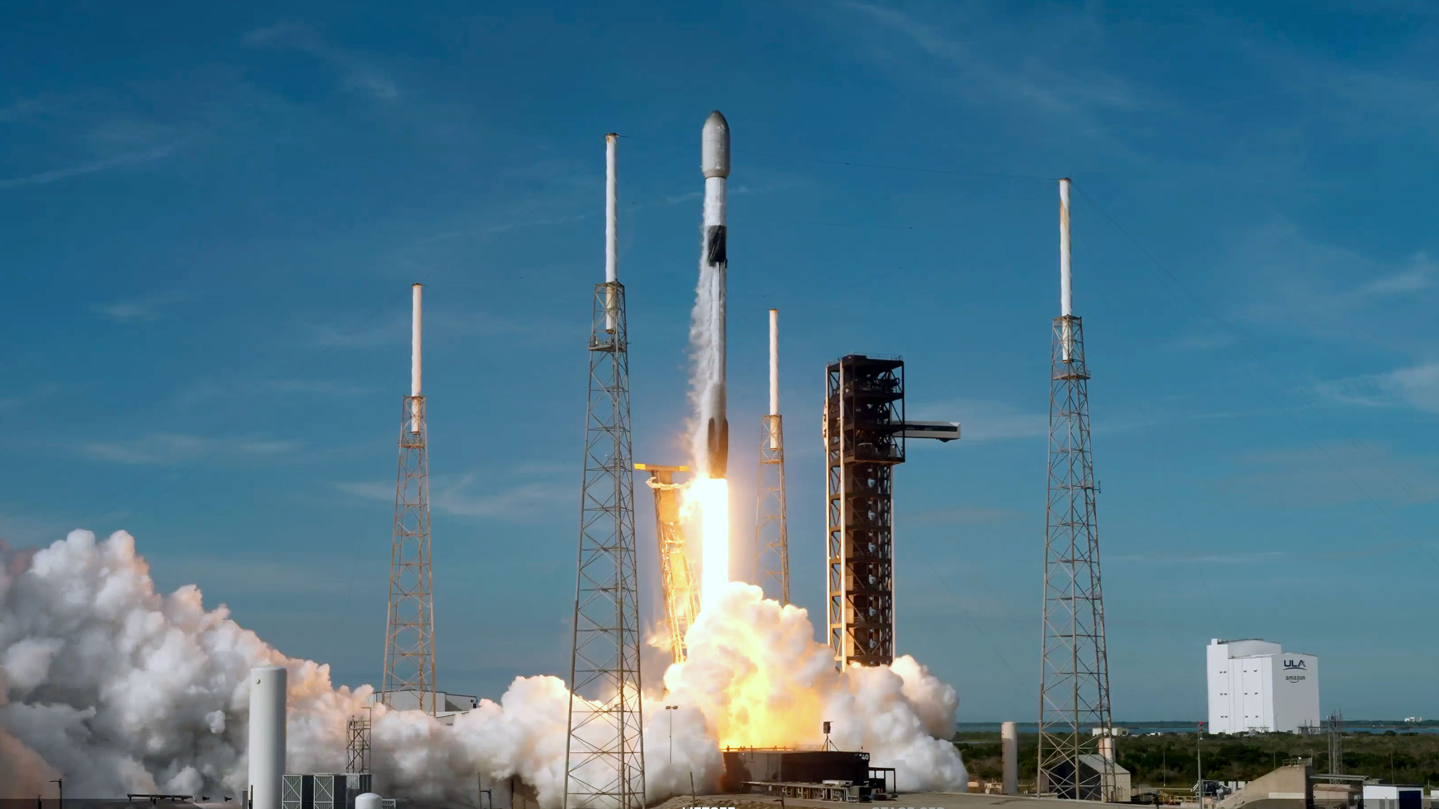A white and black rocket lifts off into a bright blue sky on its way to deploy satellites into space.