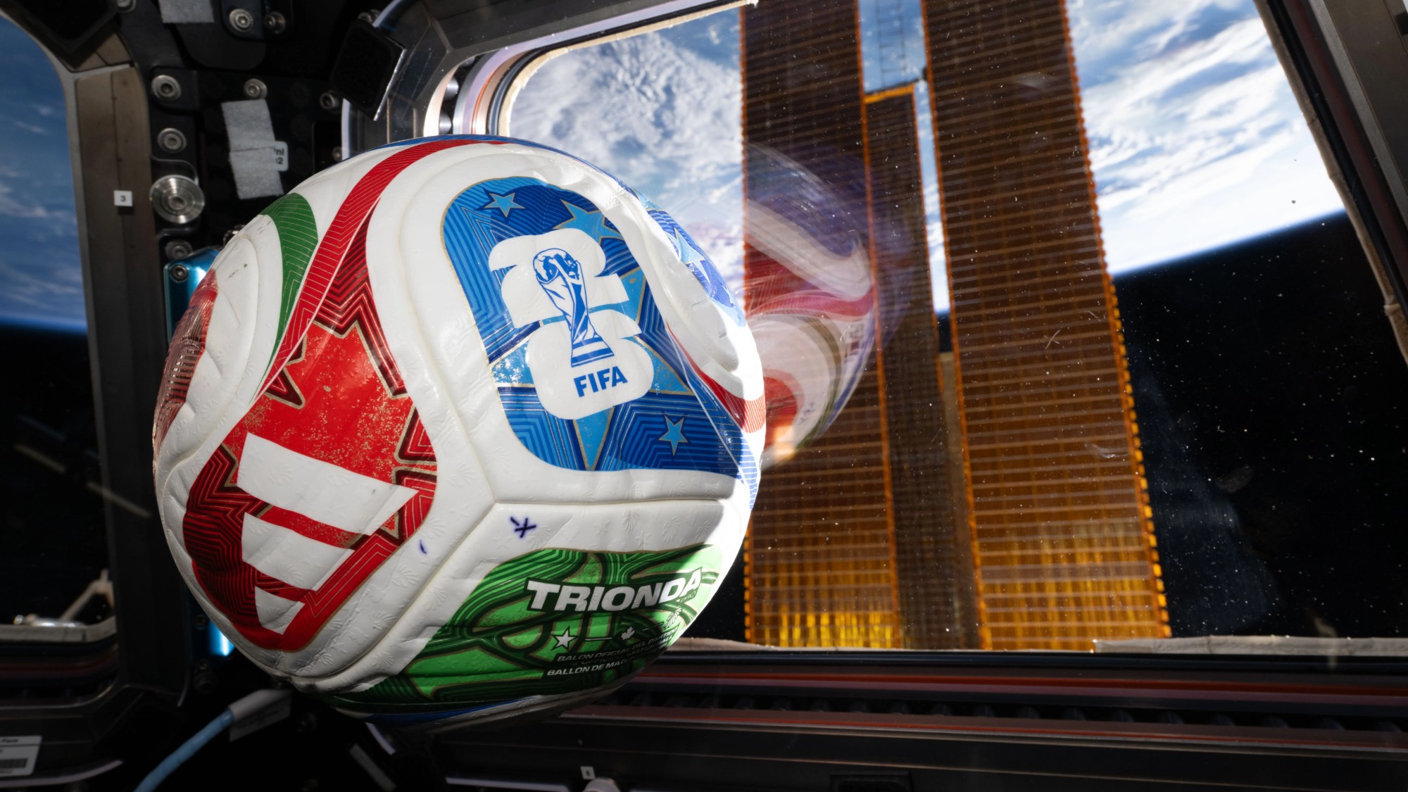 a soccer ball featuring the text 'fifa 26' sits near a window through which earth can be seen from space