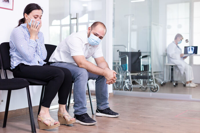 Distressed man and woman in face masks waiting in a medical industry waiting room.