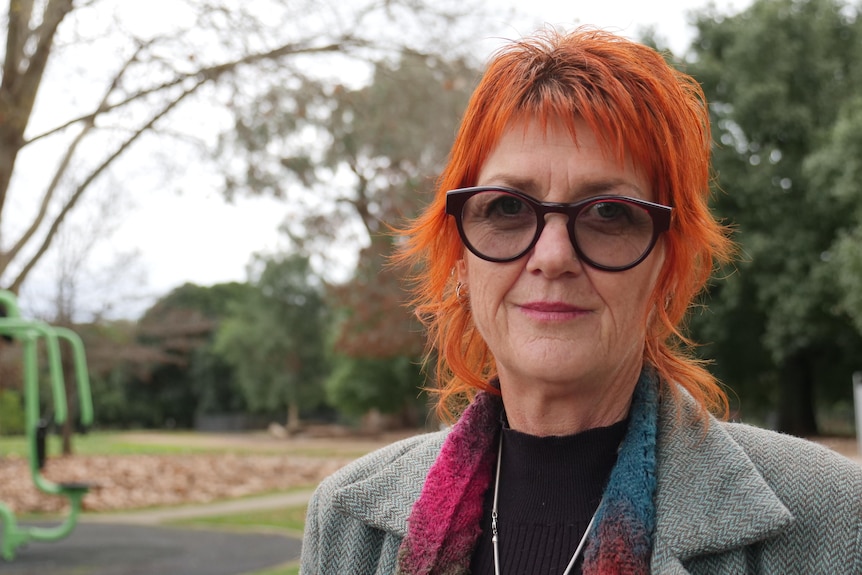 A woman with red hair looks sadly at the camera while on a park bench