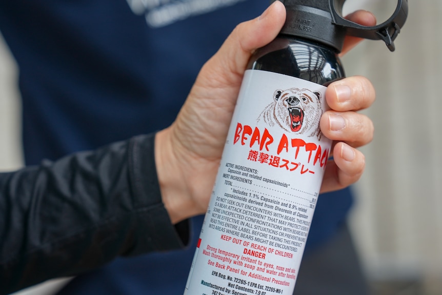 A hand on the trigger of a can that says 'bear spray' with a drawing of a bear growling