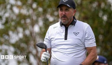 Phil Mickelson with a golf club in one hand, wearing a white shirt