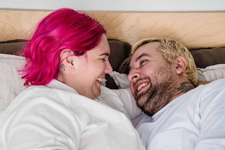 A couple in bed looking into each others eyes and laughing.