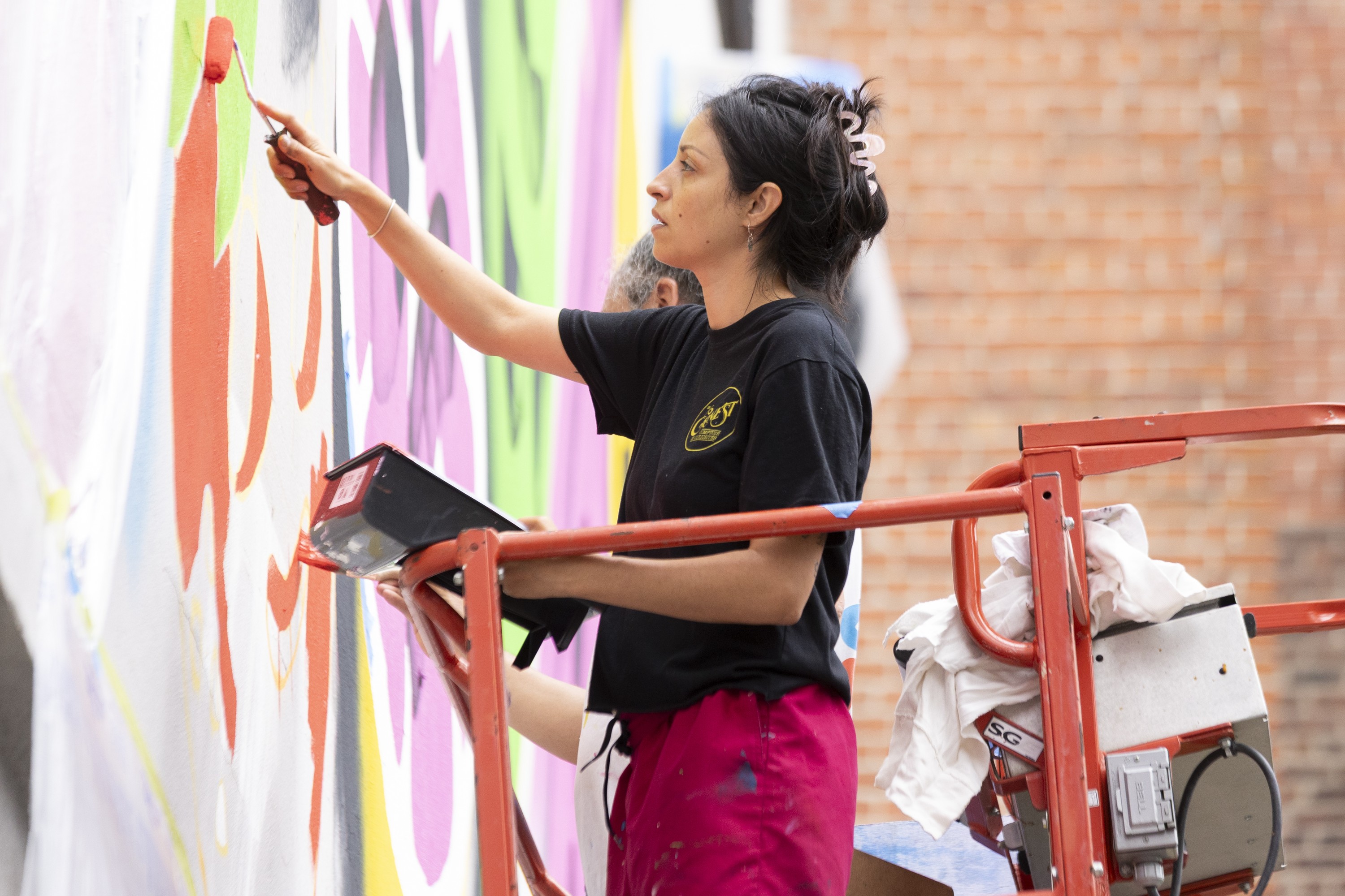 A woman paints a mural on a wall. 