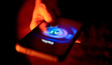 A hand touches the glowing screen of a smartphone showing an AI chatbot interface, illuminated in red and blue light.