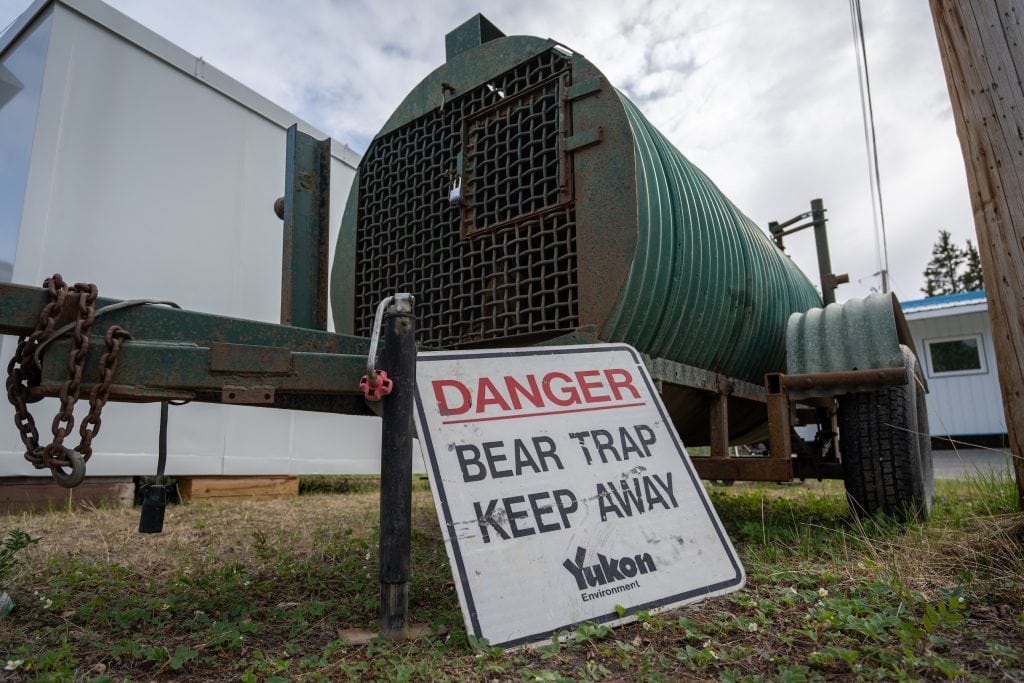 A large white sign leaning against a bear trap, reading "Danger: Bear trap keep away."