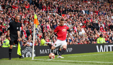 David Beckham lines up a corner kick in a crowded stadium, with a referee and assistant referee looking on near the corner flag.