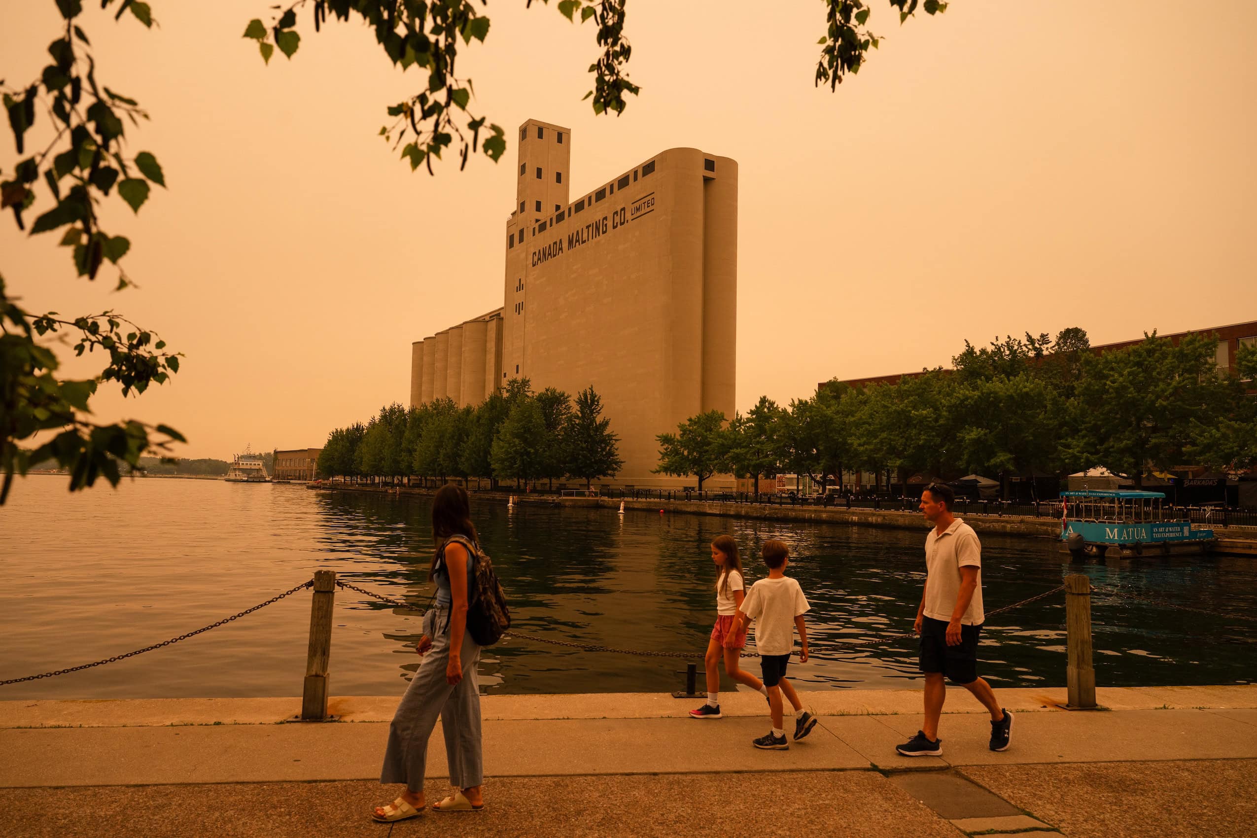 A family walks along the waterside in Toronto, amid a smoky sky.