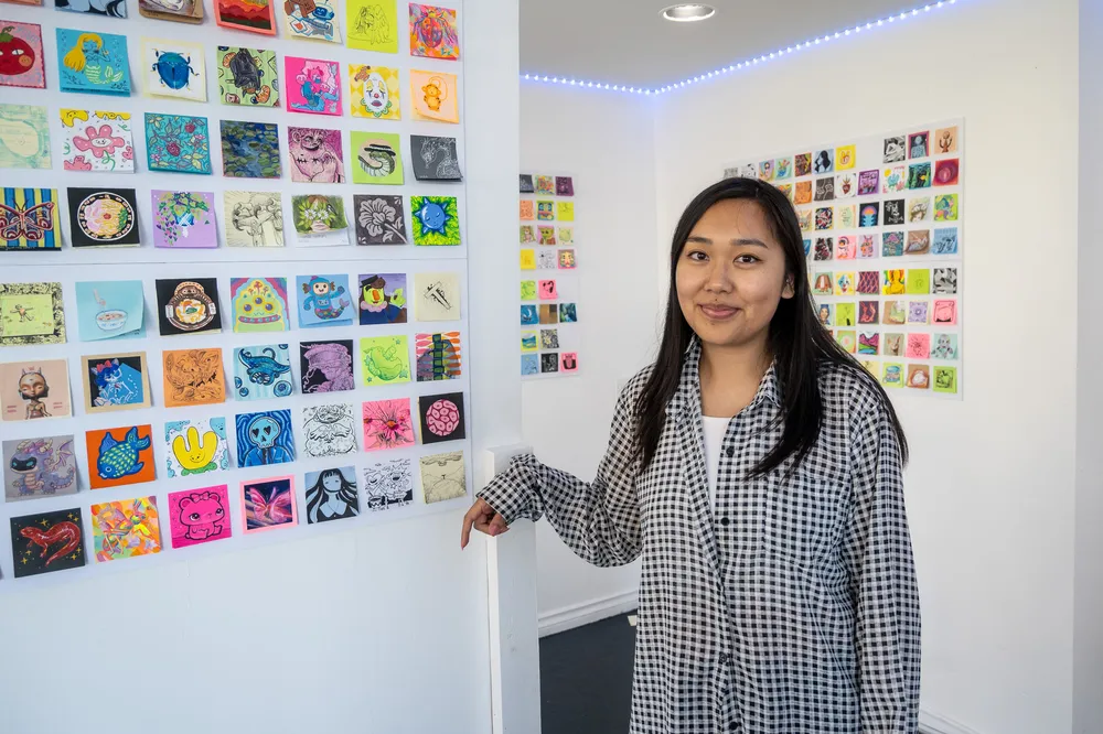 An Asian woman in a patterned shirt stands in front of some of the sticky note artwork