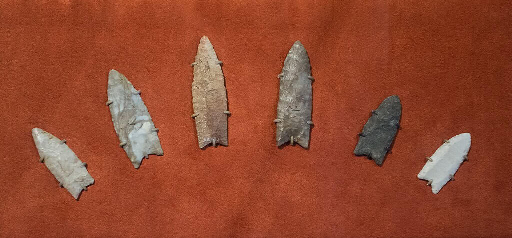 Collection of seven ancient stone arrowheads on a brown background.