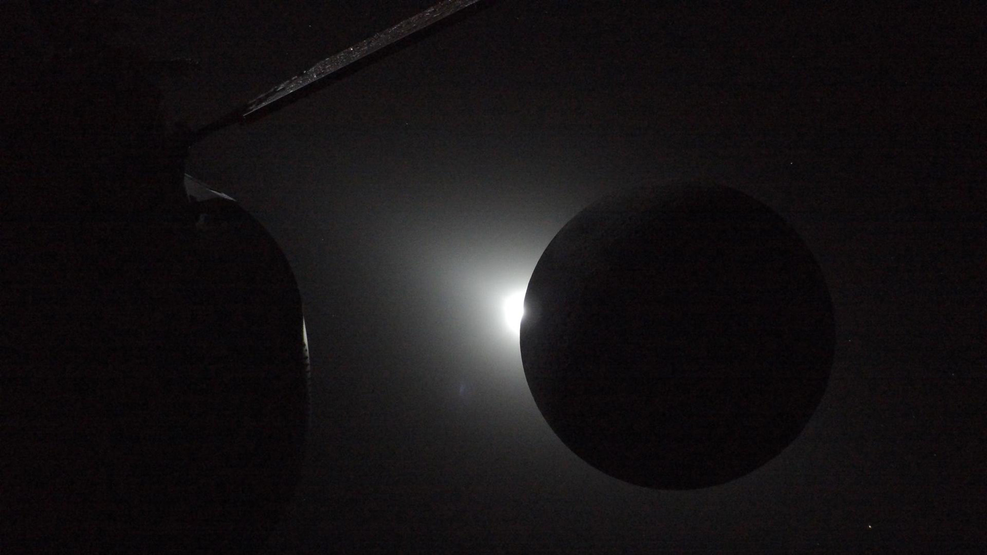 A dark sphere is seen with a glowing light peeking out behind it on its left side.
