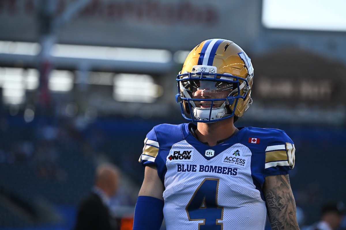 A football player wearing a Blue Bombers uniform and helmet stands on the field during a game.