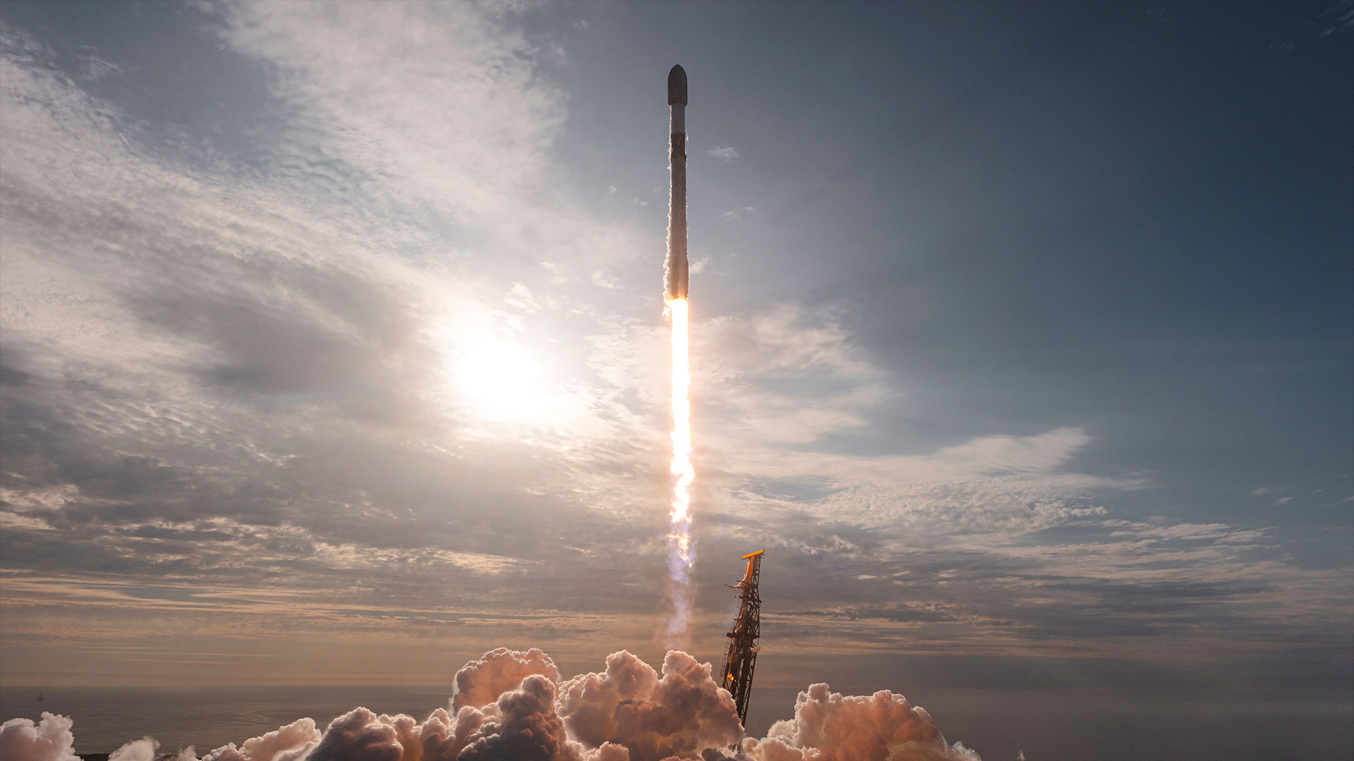a pre-dusk launch of a rocket into a partially cloudy sky