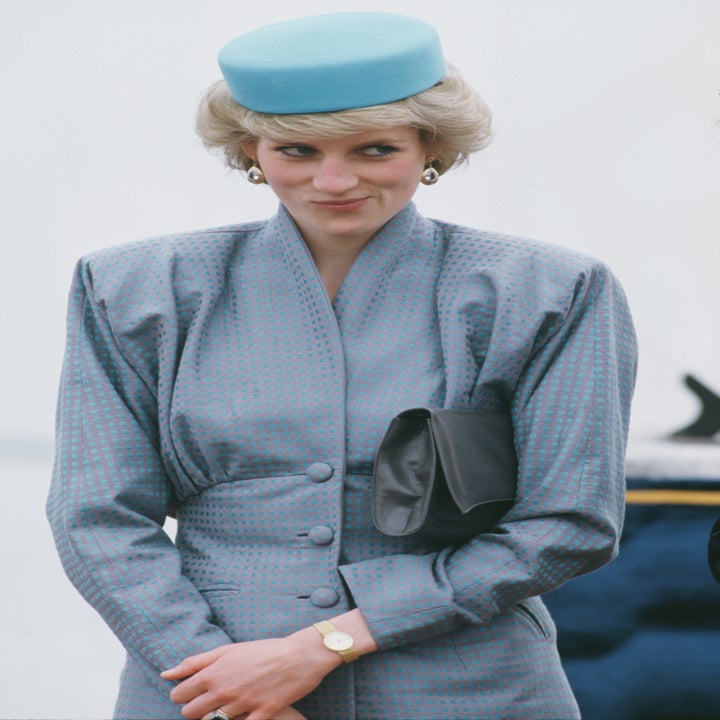 Woman on red carpet in vintage, structured suit with matching hat and clutch, displaying a playful expression