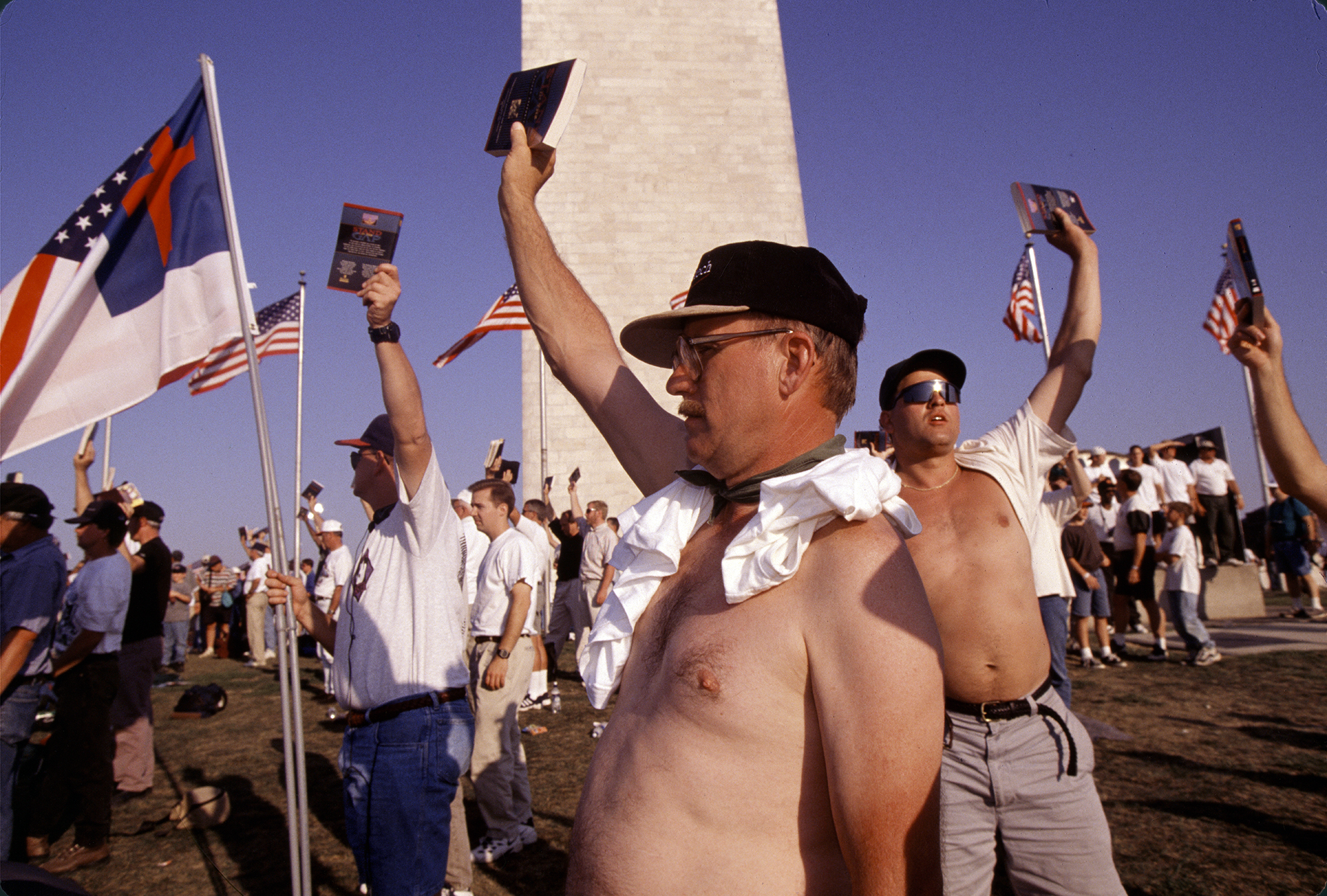 Group of men holding bibles above their heads in front of the Washington Monument.