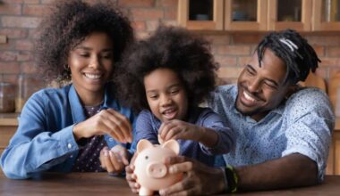 Young girl starting investing by putting a coin in a piggybank while surrounded by her parents.
