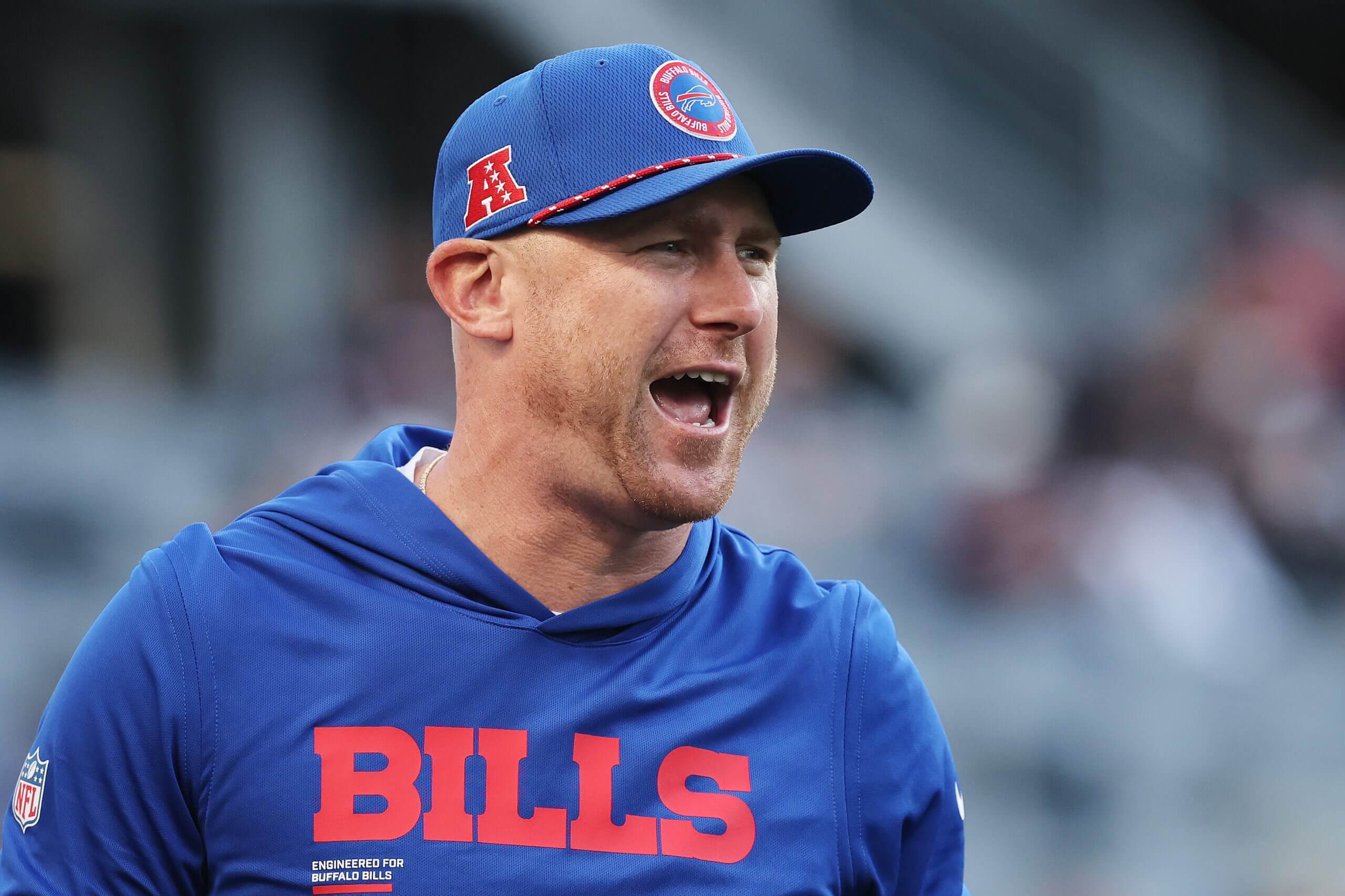Joe Brady, wearing a blue Bills hat and hoodie, looks to his left while yelling.