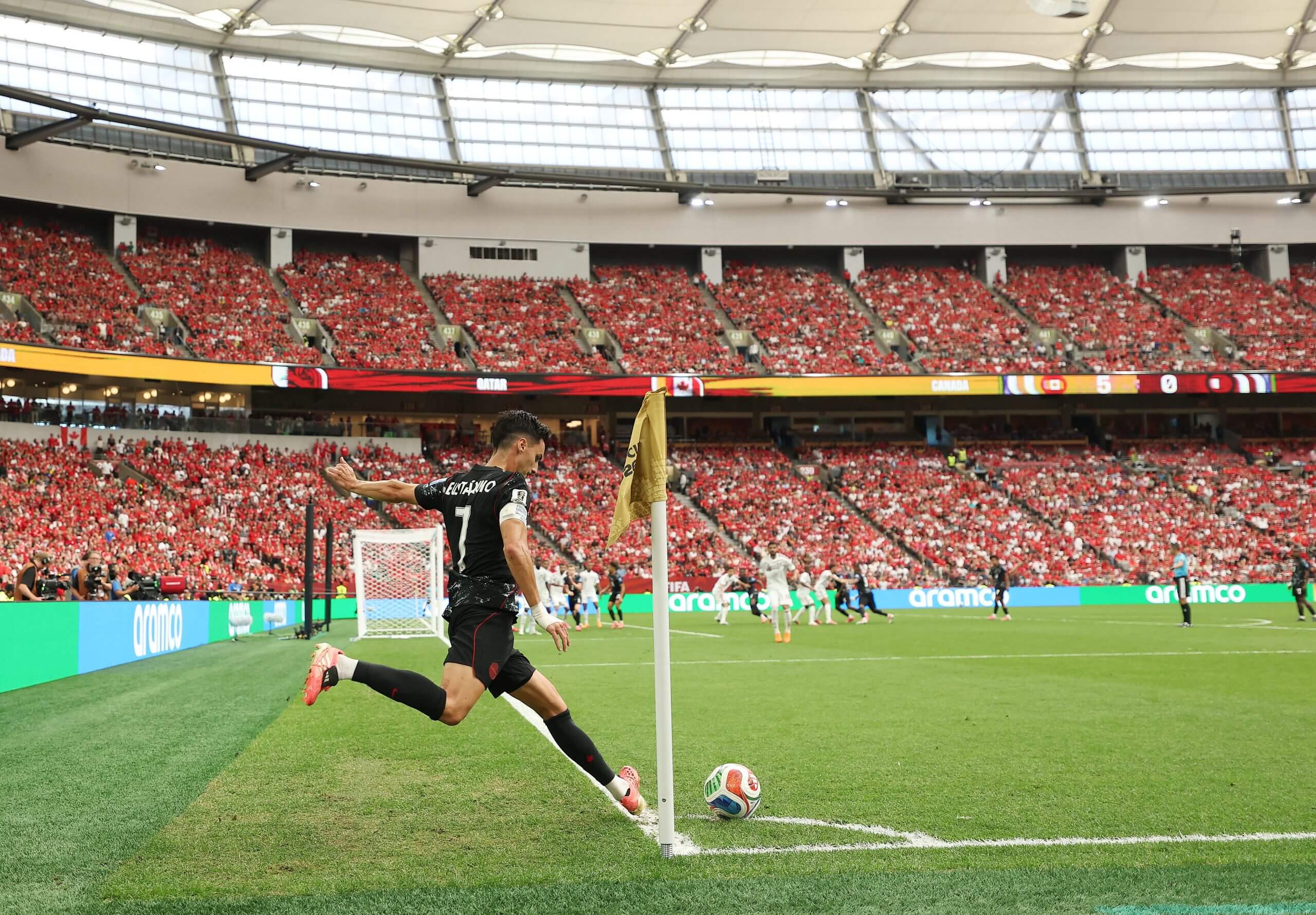 A footballer in black kit takes a corner kick with his right foot