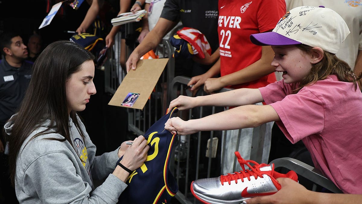 Caitlin Clark of the Indiana Fever signs autographs for fans before a WNBA game against the Phoenix Mercury.