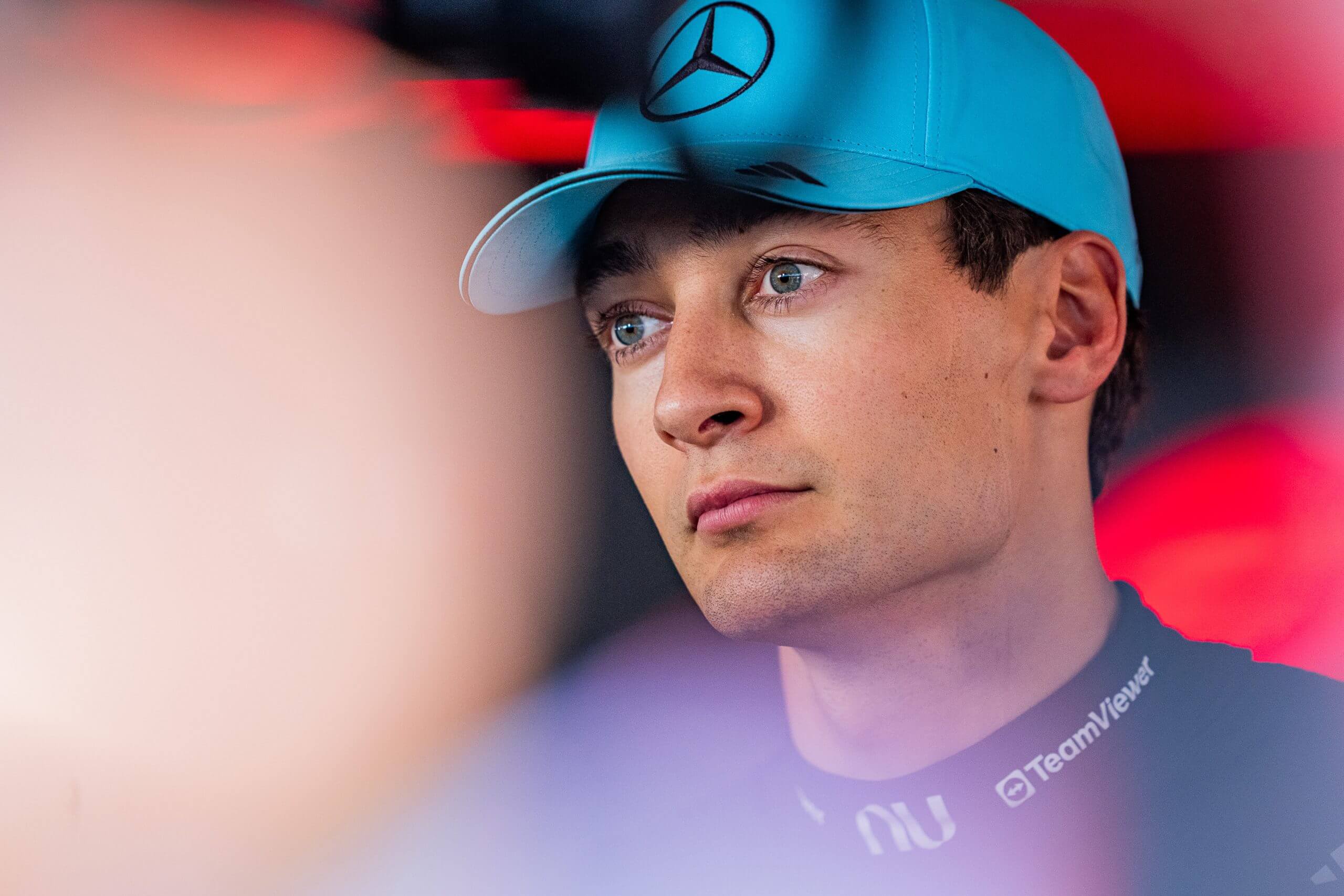 George Russell, wearing a blue cap with a Mercedes logo, looks on