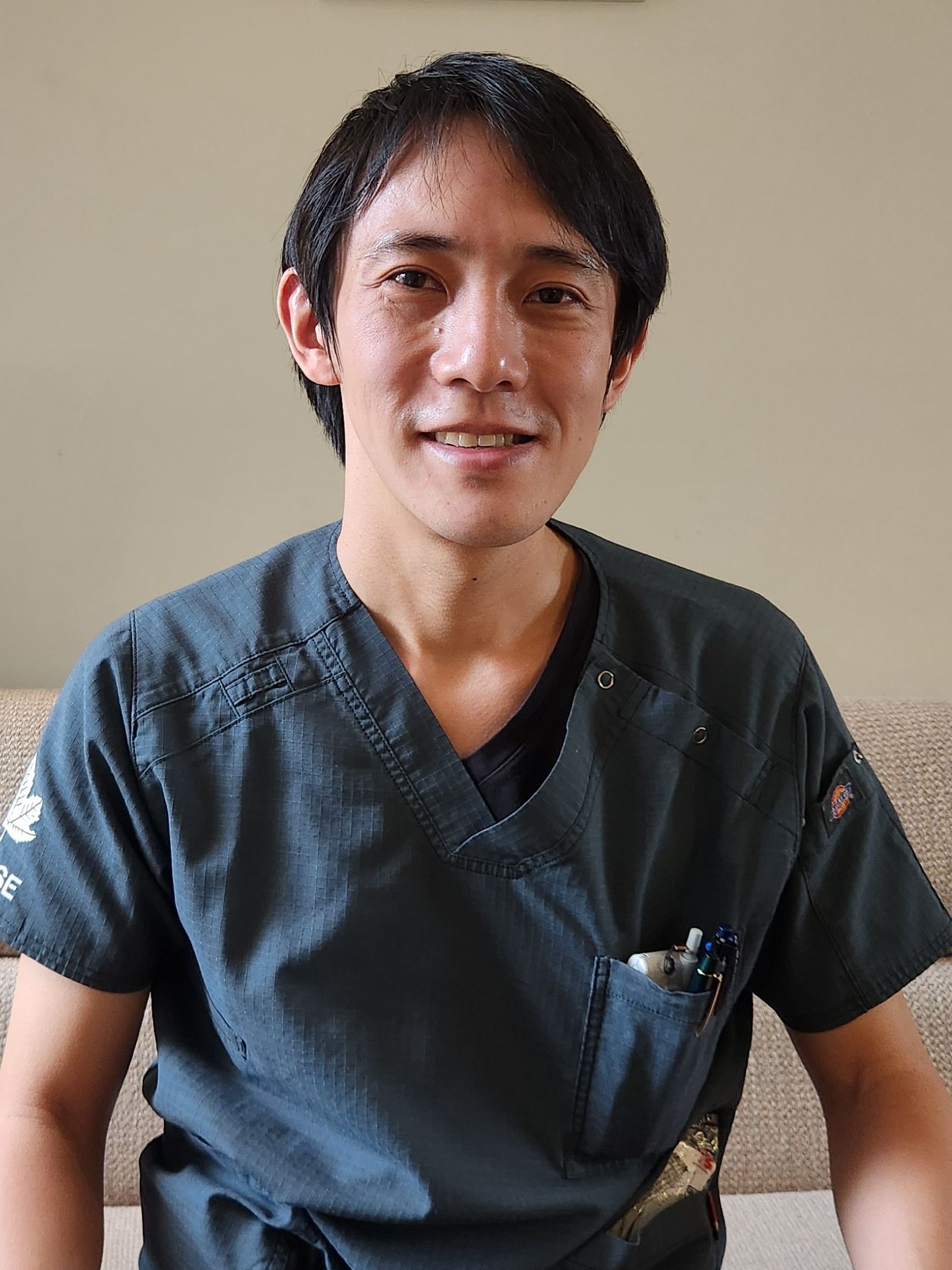 photo of a smiling man with short black hair wearing hospital scrubs