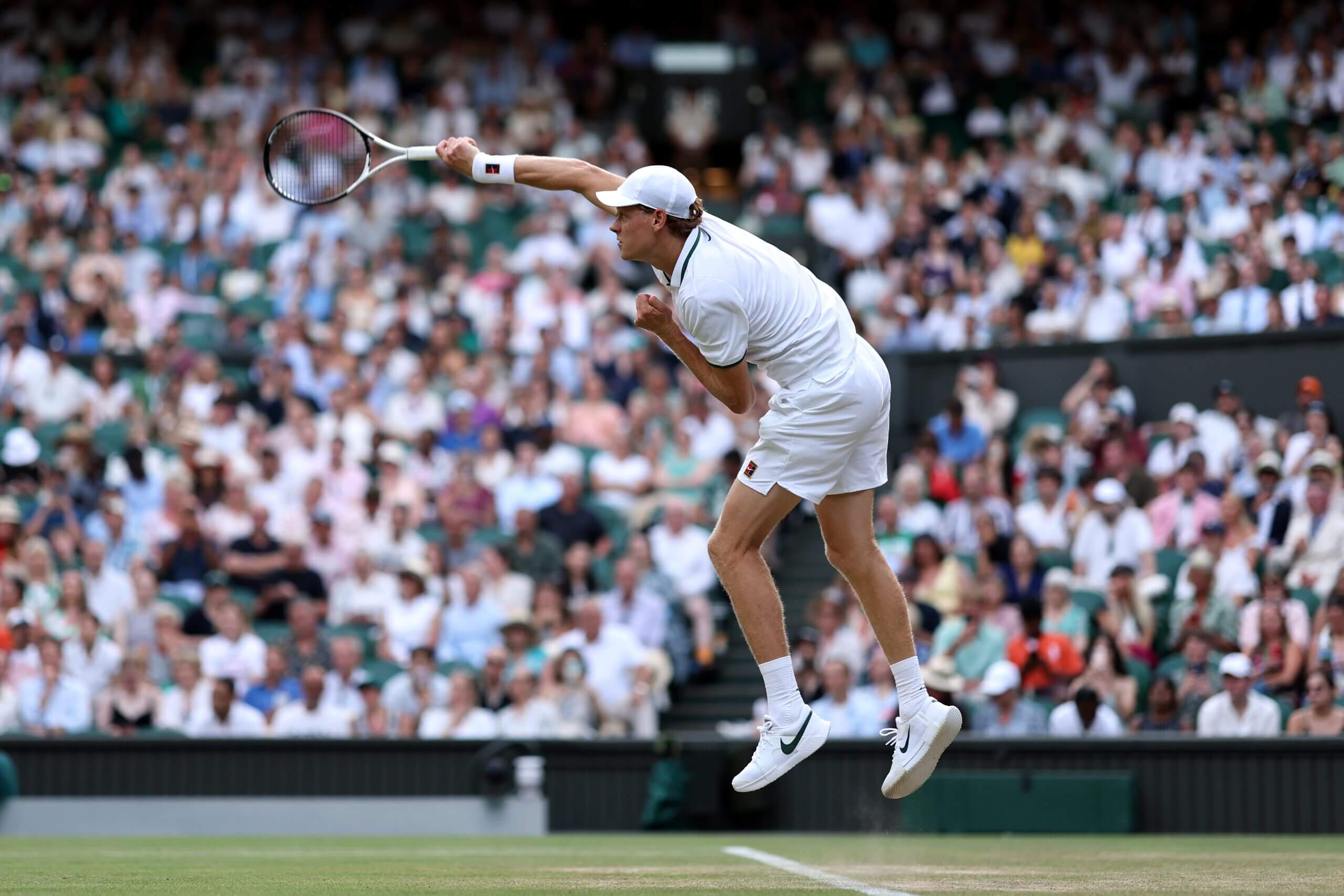 Jannik Sinner follows through on a serve in mid-air with a crowd behind him.