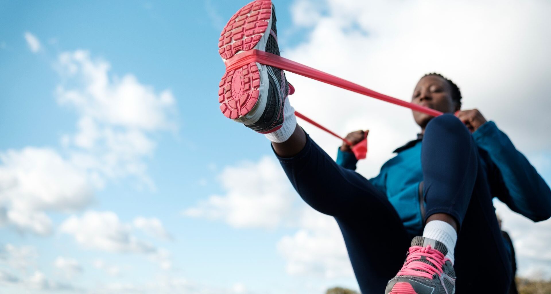 Woman doing 15-minute resistance band workout wearing activewear and trainers outside