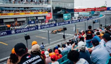 Crowded grandstand watches a race car speeding along a pit-lane street circuit with blue crypto.com banners.