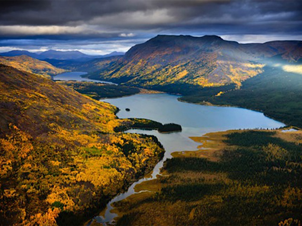 An aerial photo shows a river valley flanked on either side by fall foliage.