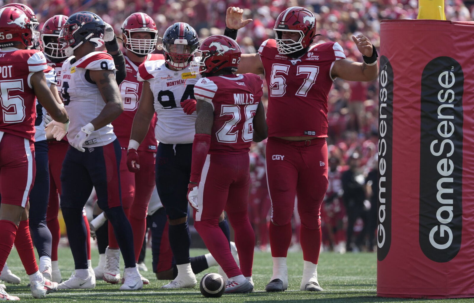 A group of football players in red and white uniforms celebrate on the field near a GameSense advertising post.