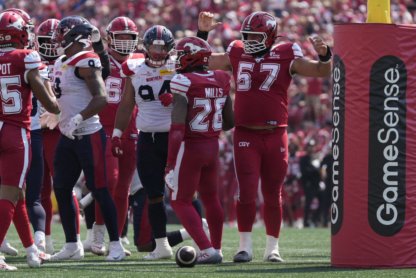 A group of football players in red and white uniforms celebrate on the field near a GameSense advertising post.