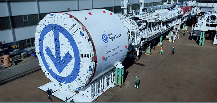 The STM's Lisette Tunnel Boring Machine in profile showing the cutterhead and elongated system for storing prefab concrete panels and conveyors for removing cut stone from the rock face.