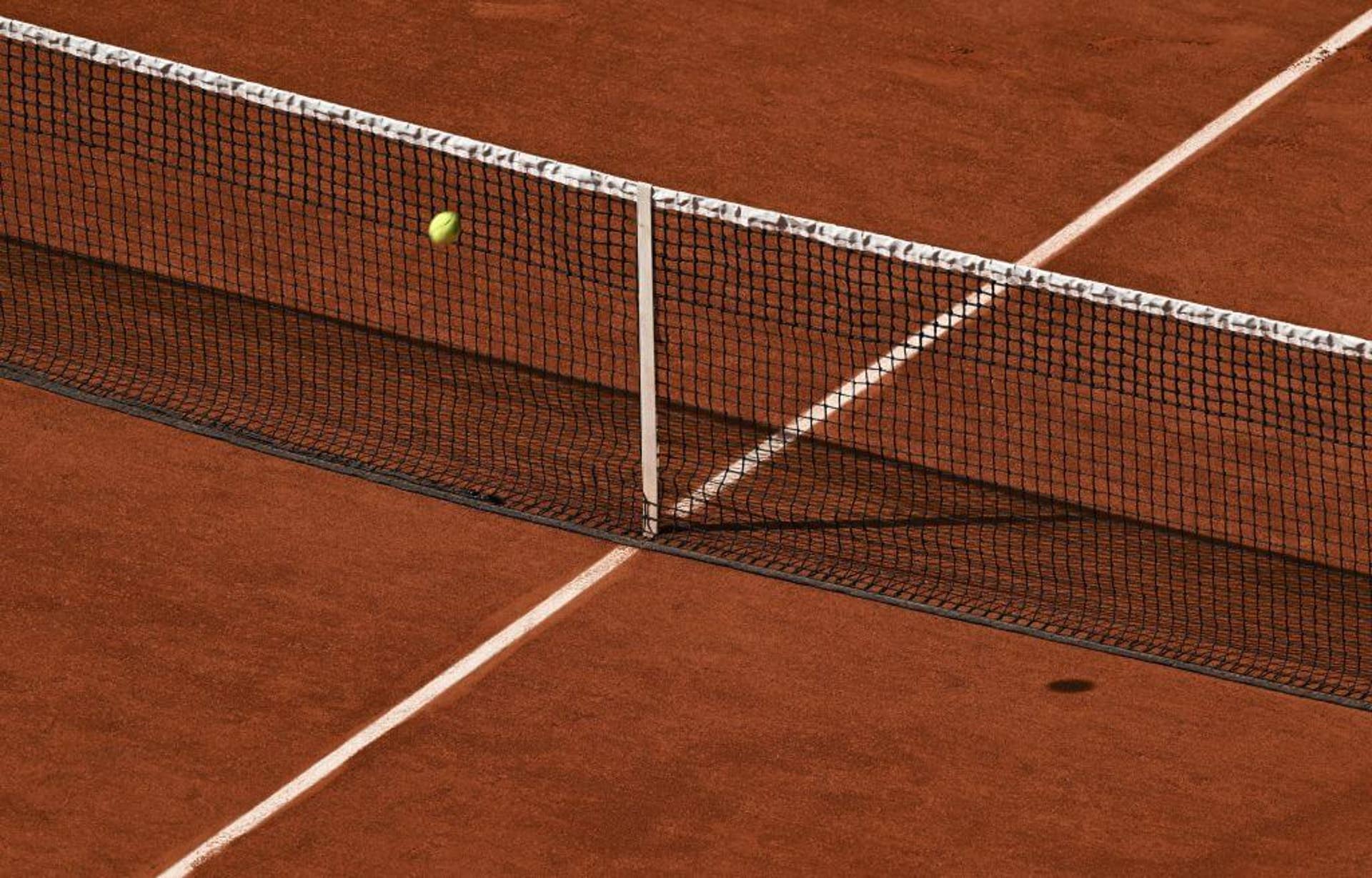 A tennis ball hits the net on a clay court.