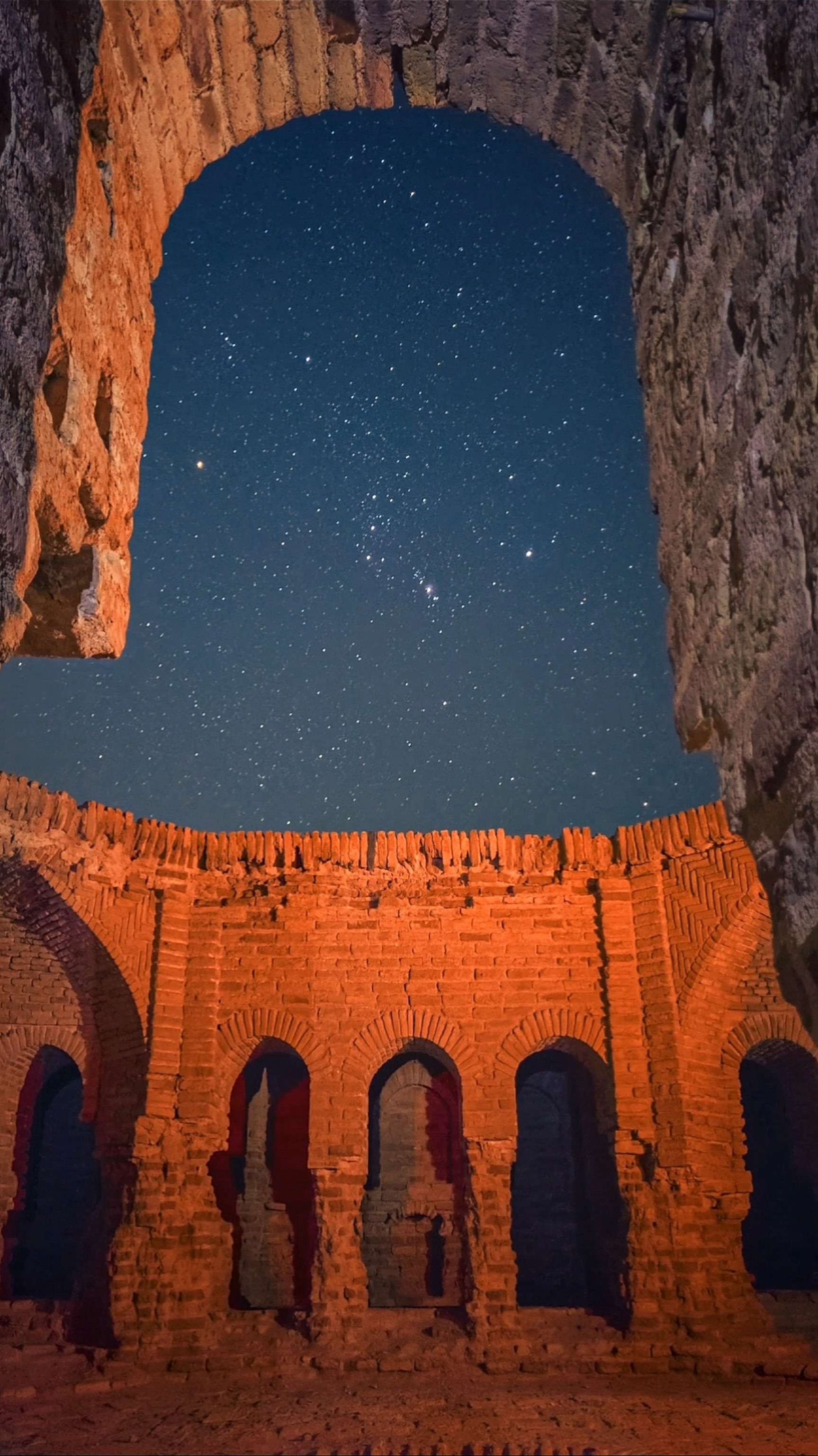 Ancient stone ruins with arched openings glowing orange under a starry night sky