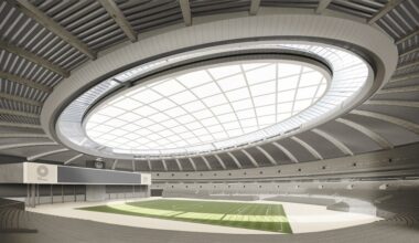Interior view of a modern stadium with a glass-paneled roof and tiered concrete seating surrounding a green playing field.