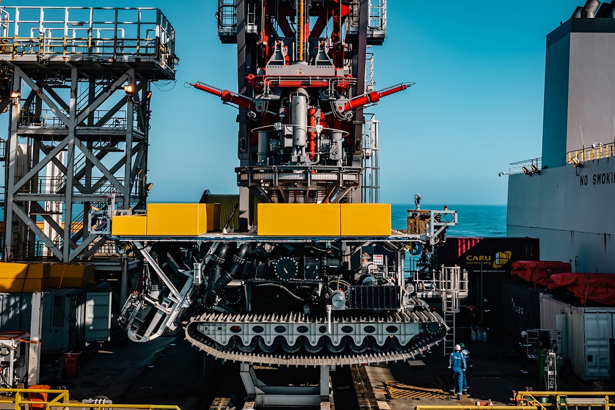 A nodule collector vechicle with tractor treads on a crane on a ship.