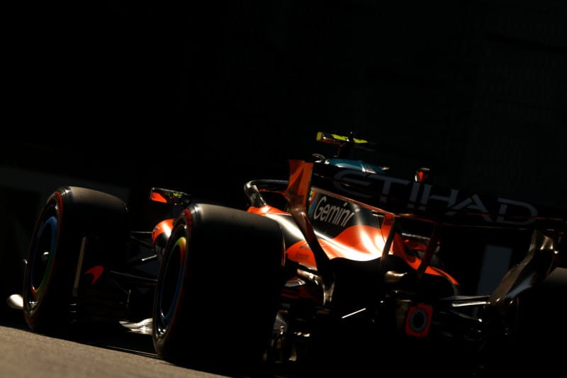 Rear three-quarter view of a red Formula 1 car on a race track at dusk, with large slick tires and rear wing visible behind the wheel arches and shadowy surroundings.