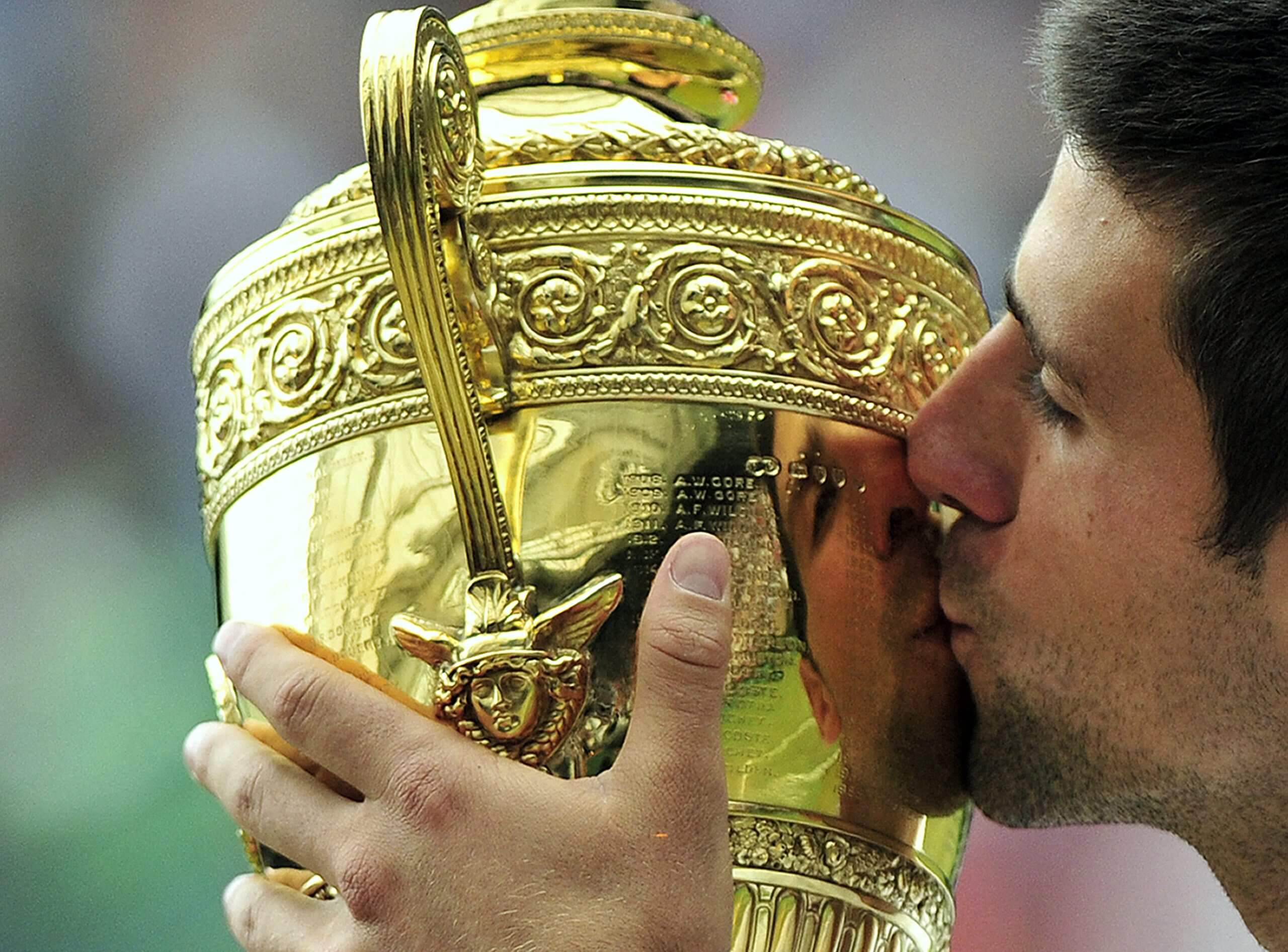 Novak Djokovic kisses the Wimbledon gentlemen's singles trophy, his face reflected in the gold.